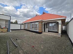 A single-story building with a red roof, large windows, and a gravel driveway. - Cozy 2-bedroom bungalow with AC in charming Nairobi (Nairobi)
