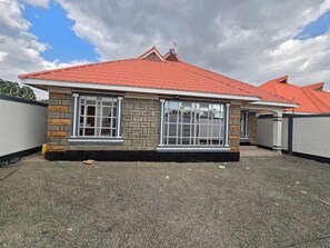 A single-story building with a red-tiled roof, large windows, and a stone facade. - Cozy 2-bedroom bungalow with AC in charming Nairobi (Nairobi)