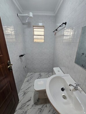 A bathroom with white tiled walls, a marble floor, a toilet, a sink, and a window. - Cozy 2-bedroom bungalow with AC in charming Nairobi (Nairobi)