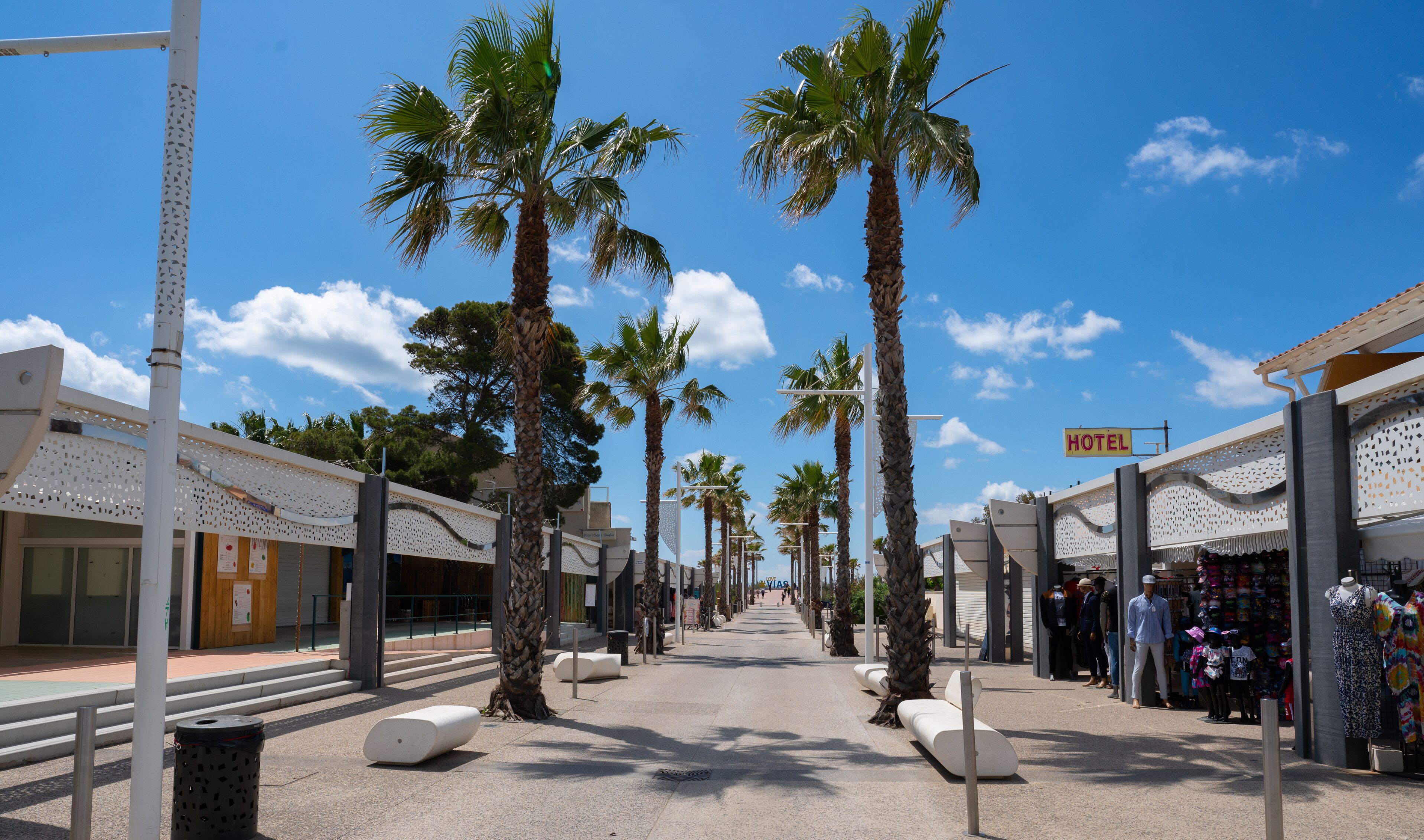 A hotel corridor with palm trees, a clear sky, and a 'HOTEL' sign.