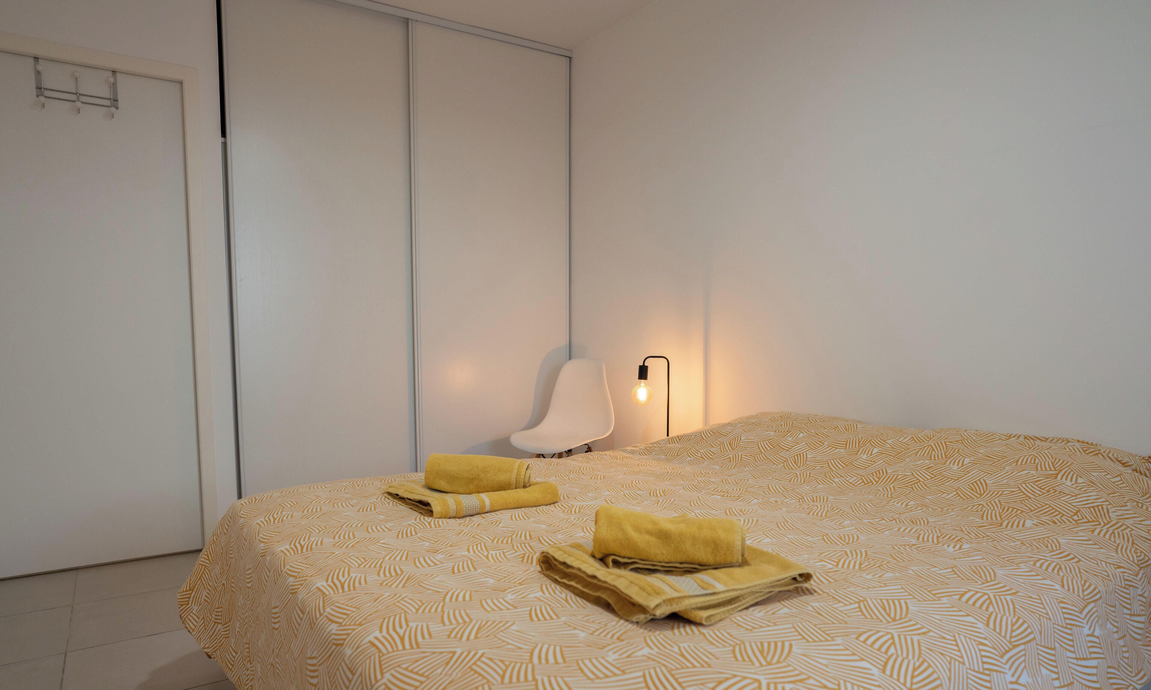 Ein Schlafzimmer mit einem Bett, einem Sessel, einer Nachttischlampe und einer Tür.