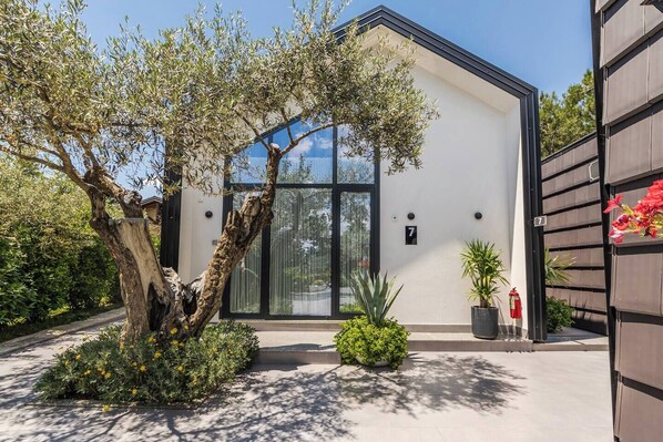 Un bâtiment moderne doté d’une grande entrée en verre, d’une enseigne avec le chiffre « 7 » et d’un arbre au premier plan.