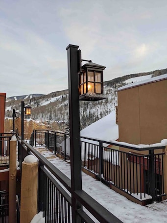 A snow-covered balcony with a railing, a lantern, and a view of a snowy landscape.. Spacious Vail Condo - 4 King Beds, Easy Bus Access