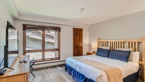 Une chambre à coucher avec un lit, un bureau avec un ordinateur, une fenêtre avec des stores et une porte.