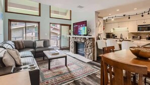 A modern living room with a fireplace, a television, and a dining area with a kitchen in the background.