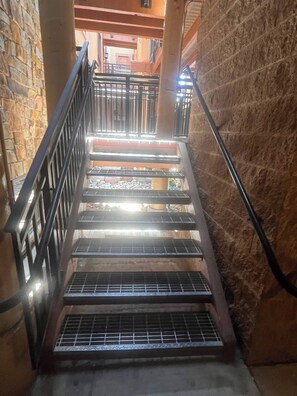 Un escalier avec des rampes en métal, des murs en pierre et une vue sur l’étage supérieur.