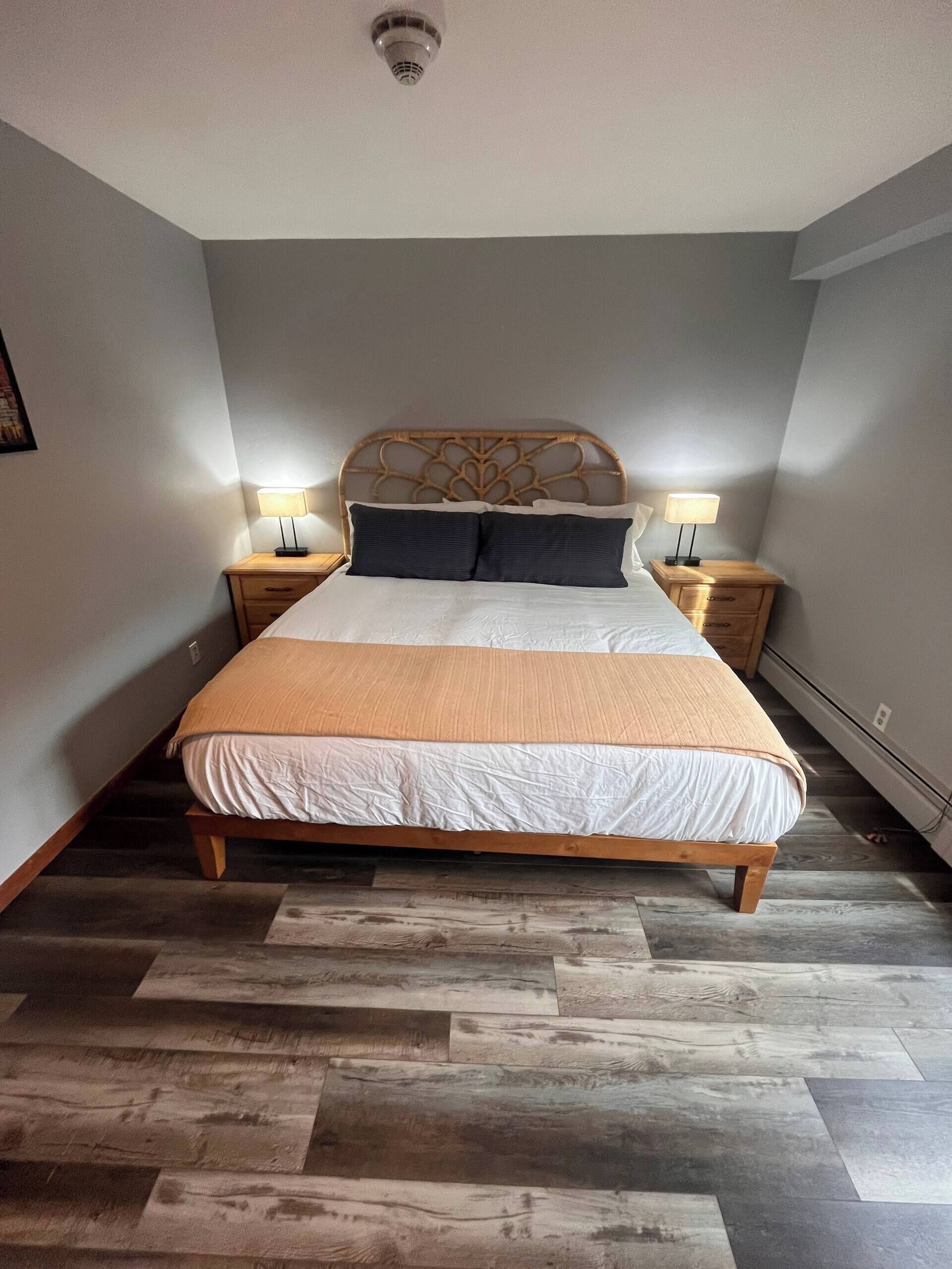 A bedroom with a bed, two bedside tables, a headboard, and a floor with wooden planks.