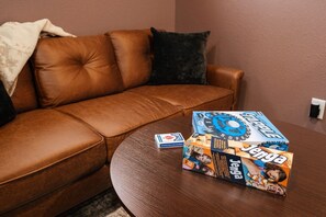 Ein braunes Ledersofa mit dunklem Kissen, ein Holztisch mit zwei Brettspielen und eine Wandsteckdose.
