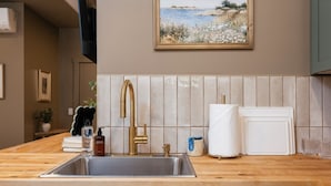 A kitchen with a sink, a gold faucet, a tiled backsplash, a painting, and a wooden countertop. - Sage Solace Studio | Near Downtown & Beaches (Traverse City)