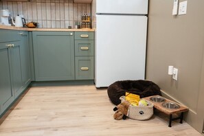 Een keuken met groene kastjes, een witte koelkast, een hondenbed en een voerbak voor huisdieren.