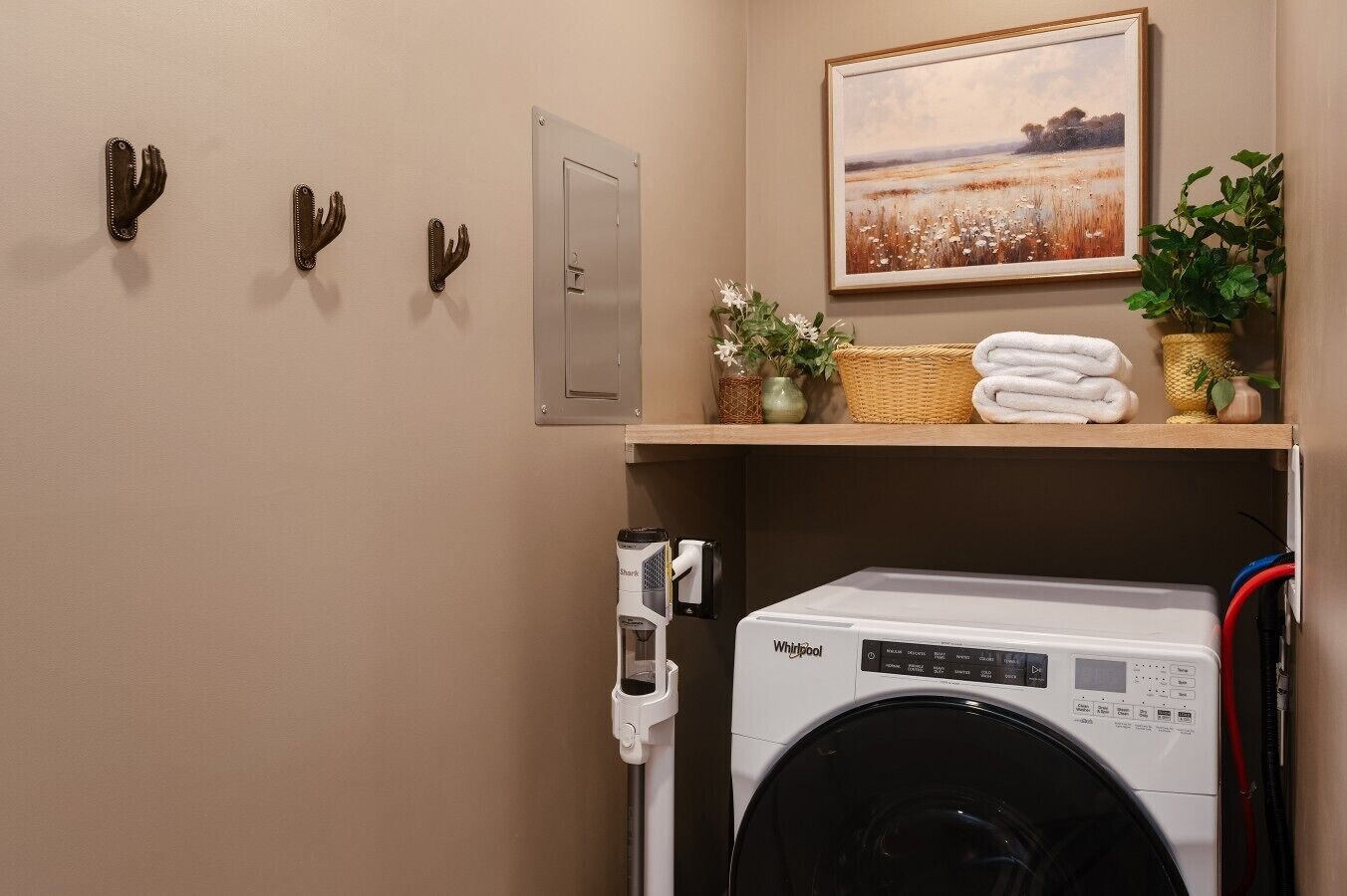Un lavadero con una lavadora Whirlpool, una puerta, un cuadro y ganchos para toallas en la pared.