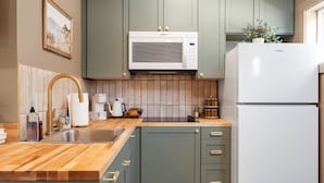 A kitchen with a wooden countertop, a stainless steel sink, a white refrigerator, and green cabinets. - Sage Solace Studio | Near Downtown & Beaches (Traverse City)