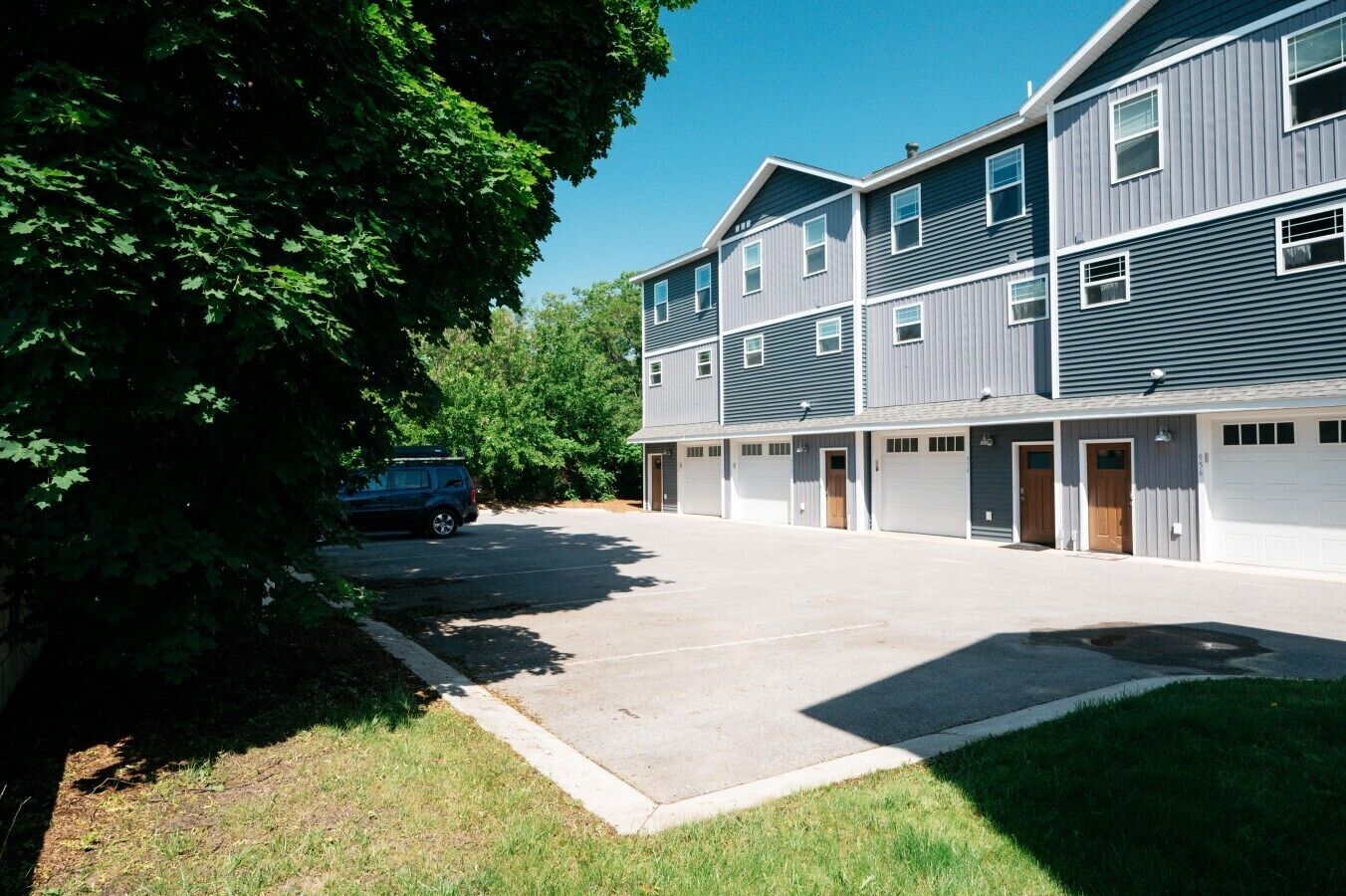 En bygning med flere etager, parkeringsplads, garageporte og et træ i forgrunden.