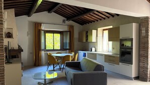 Cuina compacta amb electrodomèstics moderns, zona de dinar amb cadires grogues i un sofà gris.