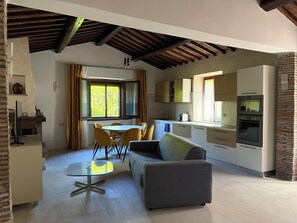 A compact kitchen with modern appliances, a dining area with yellow chairs, and a grey sofa. - Villetta immersa nel verde dell'Umbria (Umbria)