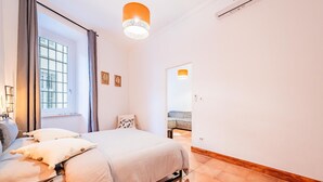 Un dormitorio con cama, ventana con cortinas, lámpara colgante y vista a otra habitación.