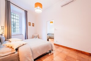 A bedroom with a bed, a window with curtains, a hanging light fixture, and a view into another room. - Apartment house "Iulia"- Pinerolo (historic center) (Pinerolo)