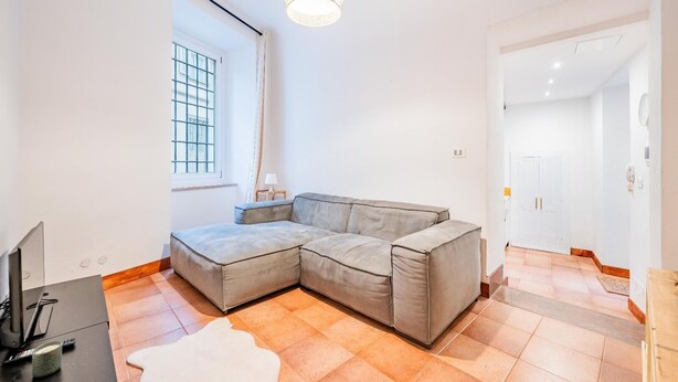 Ein modernes Wohnzimmer mit einer Eckcouch, einem Fernseher, einer Lampe und einem großen Fenster.