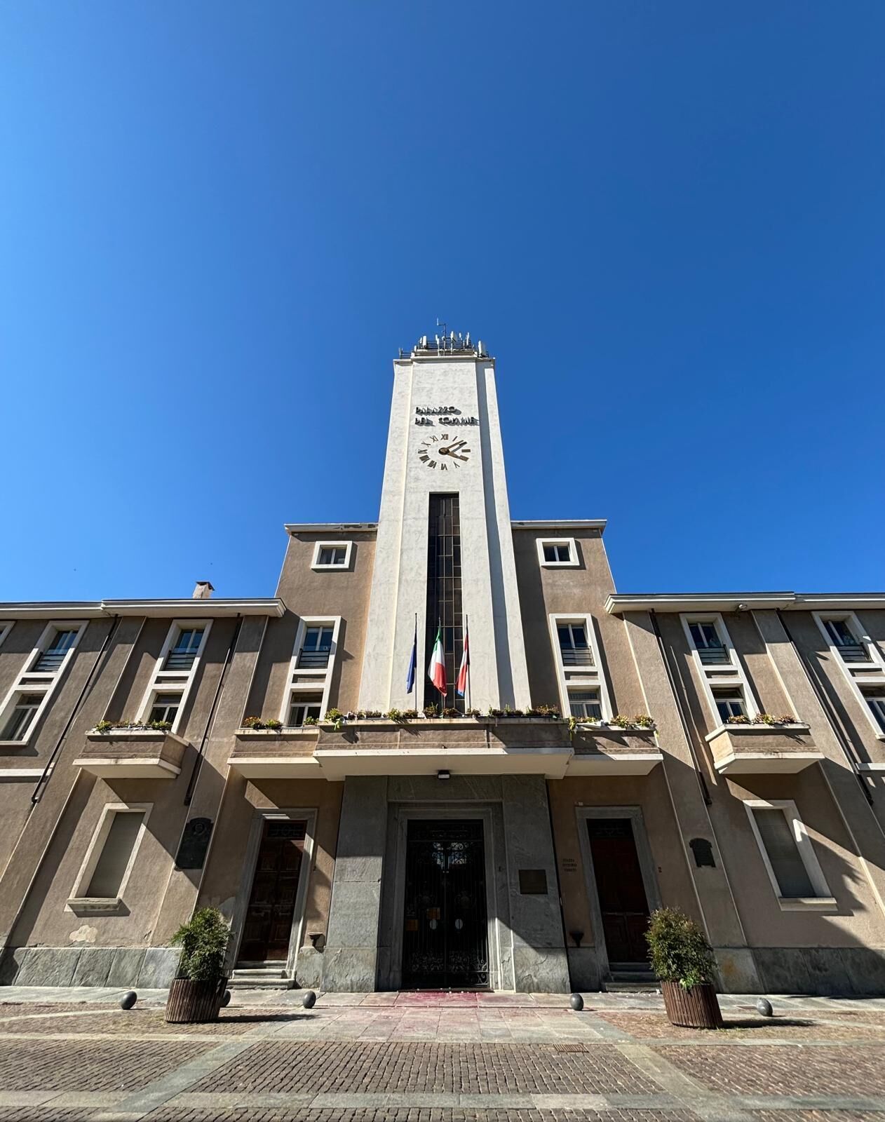 Un edificio con una torre central de reloj, una entrada principal y numerosas ventanas.