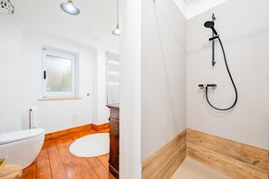 A bathroom with a toilet, a wooden floor, a white rug, a window, and a shower with a wooden base. - Apartment house "Iulia"- Pinerolo (historic center) (Pinerolo)