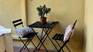 Eine kleine Terrasse mit Tisch und Stühlen, einem Blumentopf und einem Fenster mit Rollläden.