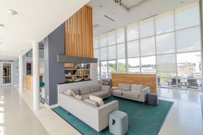 A spacious lobby with a large seating area, a wooden accent wall, and large windows offering a view of the outdoors. - Stunning unit with great amenities (Columbus)