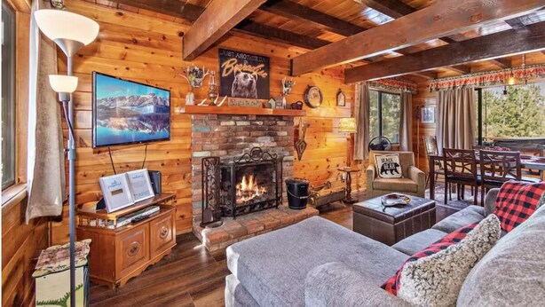 Ein gemütliches Blockhausszenario mit Kamin, Holzwänden, Fernseher und Essbereich.