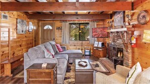 Ein Blockhaus-Interieur mit Kamin, Holzwänden, einer Couch und einem Fernseher.