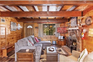 A log cabin interior with a fireplace, wooden walls, a sofa, and a television. - Peek-A-Boo Lake View, Dog Yard, Near Village (Big Bear Lake)