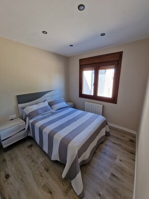 Een slaapkamer met een bed, nachtkastje, raam en radiator.