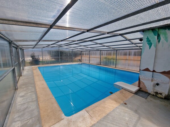 A covered swimming pool with a glass ceiling, a ladder, and a bench.