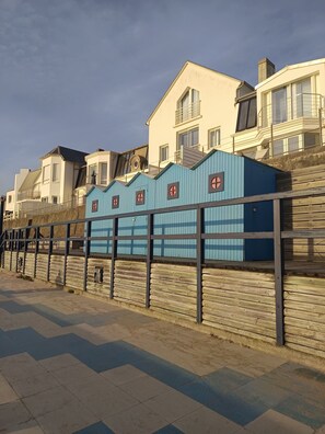 Ein Küstengebäude mit blauer Fassade, einer Holzterrasse und einem Metallgeländer.