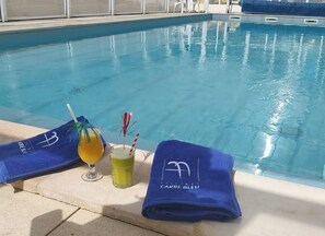 Ein Poolbereich mit Handtuch, einem Glas mit gelber Flüssigkeit und einem Glas mit Trinkhalm und einem roten und weißen Streifenmuster.