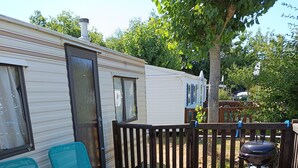 A wooden deck with two green lounge chairs, a barbecue grill, and a wooden fence. - Vendée getaway: Mobil home _ Commequiers (Commequiers)