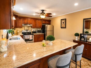 A kitchen with wooden cabinets, a granite countertop, a ceiling fan, and a refrigerator.