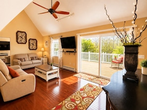 A living room with a ceiling fan, a sofa, a coffee table, a TV, and a sliding glass door leading to an outdoor deck.