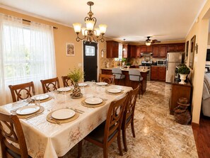 A dining area with a table set for six, wooden chairs, a chandelier, and a kitchen in the background.