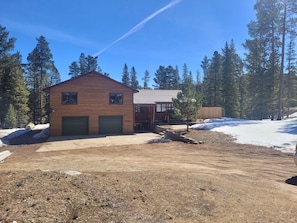 A wooden cabin with two garages, a covered porch, and a snow-covered ground. - Spacious Hillside Cabin Near Slopes (Lead)
