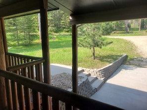 A wooden deck with a stone wall and steps leading to a grassy area with trees. - Spacious Hillside Cabin Near Slopes (Lead)