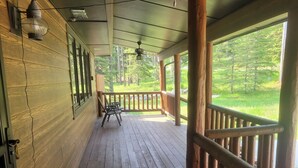 Eine Holzterrasse mit Geländer, einem Stuhl und Blick auf einen Wald.