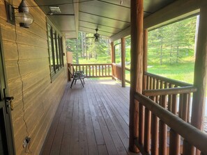 A wooden deck with a railing, a chair, and a view of a forest. - Spacious Hillside Cabin Near Slopes (Lead)