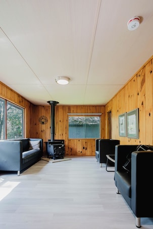 A cabin interior with a wood-paneled wall, a fireplace, two sofas, and a ceiling light.. 3-Bedroom Cottage #5