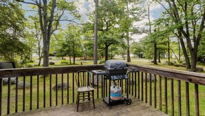 A wooden deck with a grill, a chair, and a gas tank. - 3-Bedroom Cottage #5 (Nobel)