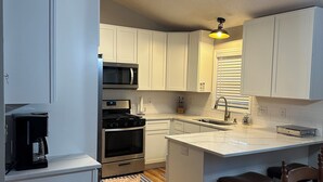 Une cuisine moderne avec des meubles blancs, un îlot central, un four à micro-ondes, un four traditionnel et une machine à café.
