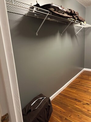 Ein Zimmer mit grauer Wand, Holzboden, einem Metallregal mit Kleidung und einer Tasche auf dem Boden.