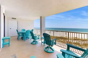 Ein Balkon mit türkisfarbenen Stühlen und einem Tisch mit Blick auf einen Strand.