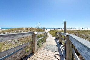 Ein hölzerner Steg führt zu einem Strand bei klarem Himmel.