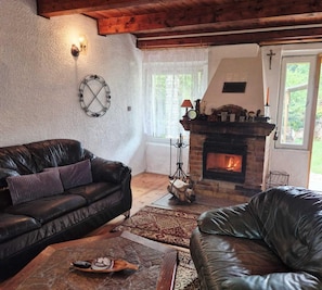 A cozy living room with a fireplace, leather sofas, a stone coffee table, and a rustic wooden ceiling. - Lakeside Holiday Villa, Private Garden (Szczecinek)