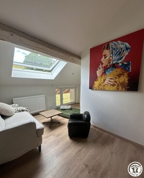 Een moderne woonkamer met dakraam, een schilderij, een bank, een salontafel en een fauteuil.