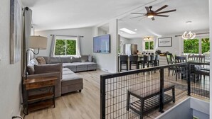 A spacious living area with a grey sectional sofa, a wooden coffee table, and a dining area with a glass table and chairs. - Arbor House - A House for Families & Friends (Lyndon Station)